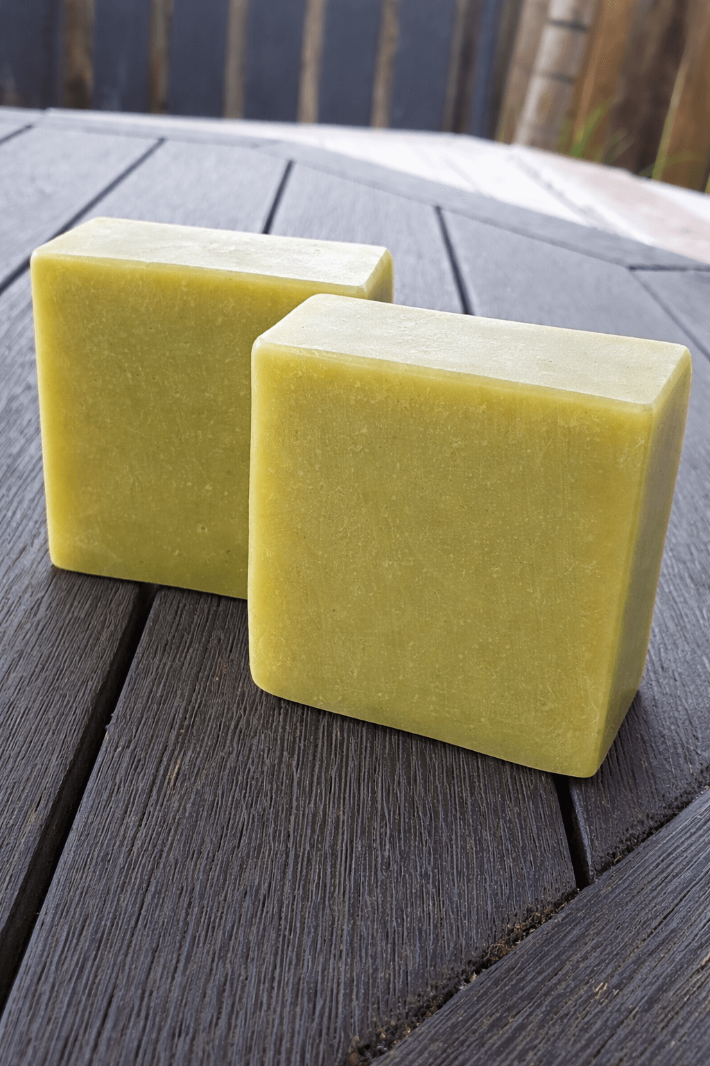 Two pieces of lemongrass tallow soap on a wooden table, showcasing their green color and handcrafted design.