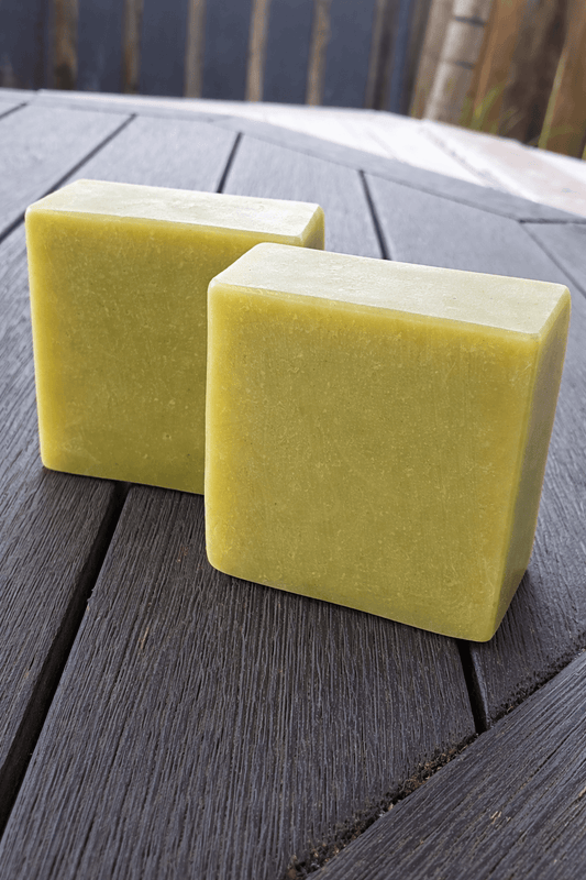 Two pieces of lemongrass tallow soap on a wooden table, showcasing their green color and handcrafted design.
