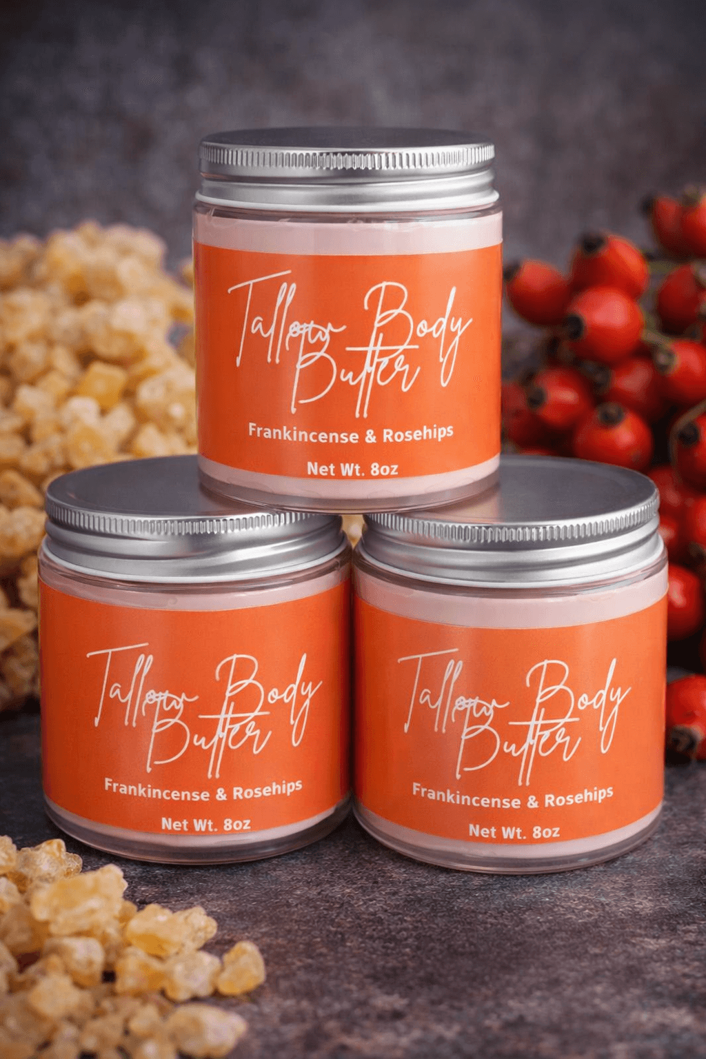 Three jars of Tallow Body Butter with labels showing frankincense and rosehips, surrounded by natural ingredients.